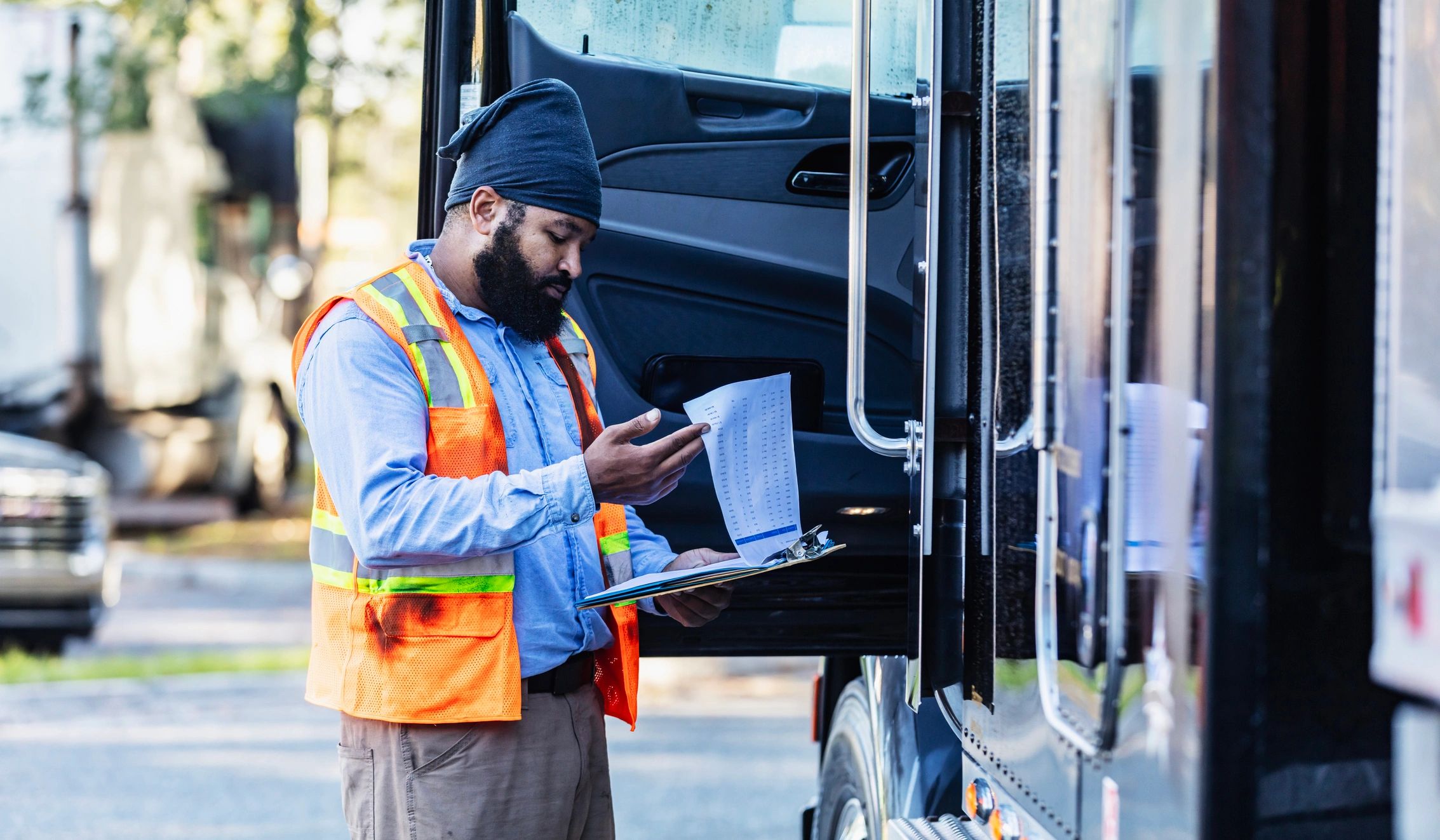 Truck driver standing beside a semi-truck with a clipboard